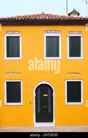 Facciata in stucco giallo con porta d'ingresso ad arco marrone e finestre chiuse, Isola di Burano, Laguna di Venezia, Venezia, Veneto, Italia. Foto Stock