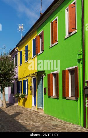 Facciate verdi, gialle e rosa con persiane temporesche su finestre e marciapiede in pietra, Isola di Burano, Laguna di Venezia, Venezia, Veneto, Italia. Foto Stock