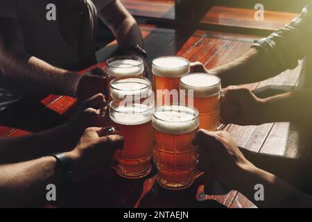 Amici che si aggraffano i bicchieri con la birra al tavolo, primo piano Foto Stock