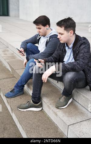 Due antisociale di telefono cellulare di tossicodipendenti adolescenti maschi guardando smartphone durante l udienza del fuori starircase - concetto di tecnologia Foto Stock