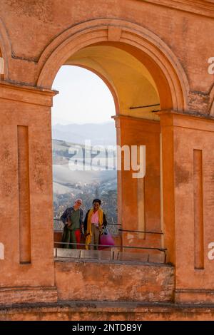 Coppia sorridente alla macchina fotografica attraverso l'arco di Portico di San Luca, Santuario della Madonna di San Luca, Bologna, Emilia-Romagna, Italia Foto Stock