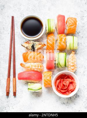 Un assortimento di sushi set su cemento bianco sullo sfondo. I sushi giapponesi La cucina, rotoli, la salsa di soia, lo zenzero, i bastoncini. Vista dall'alto. Il nigiri sushi. Giapponese pranzo/cena. Foto Stock