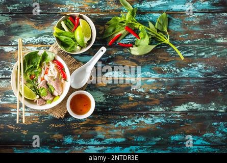 Tradizionale zuppa vietnamita Pho bo con erbe aromatiche, di carne o di riso tagliatelle, brodo. Pho bo nella ciotola con bacchette, cucchiaio. Spazio per il testo. Vista dall'alto. Zuppa asiatica Foto Stock