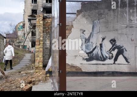 Borodyanka, Ucraina. 26th Feb, 2023. Una donna cammina vicino al lavoro di Banksy, il lavoro dell'artista inglese Banksy è visibile su un muro distrutto, dopo che la Federazione russa ha attaccato la città di Borodyanka, le autorità hanno deciso di salvare il lavoro di Banksy e ora sono protetti dal sistema. Credit: SOPA Images Limited/Alamy Live News Foto Stock