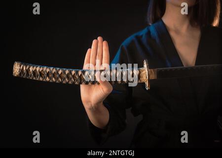 Primo piano sull'ilta di una spada katana in mano a una donna in un kimono nero Foto Stock