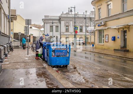 Mosca. Russia. Febbraio 25, 2023. Una donna mendicante scava attraverso i bidoni dei rifiuti in via Perechistenka a Mosca in una giornata invernale. Foto Stock