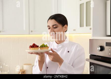 Buon pasticcere professionale con deliziose tartine in cucina Foto Stock