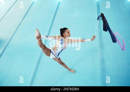 Ginnastica, donna con nastro per danza e performance, flessibilità con atleta professionista in palestra e vista dall'alto. Ginnastica ritmica, gamba in aria con Foto Stock