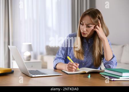Giovane donna confusa che guarda il webinar al tavolo in camera Foto Stock