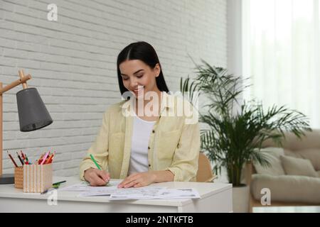 Giovane donna colorazione antistress pagina alla scrivania al coperto Foto Stock