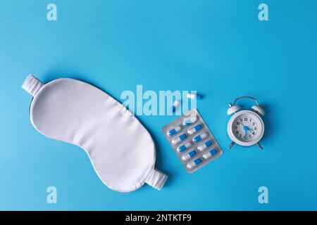 Maschera per dormire, pillole e sveglia su sfondo azzurro, piatto. Trattamento dell'insonnia Foto Stock