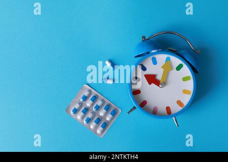 Sveglia e pillole su sfondo azzurro, piatto. Trattamento dell'insonnia Foto Stock