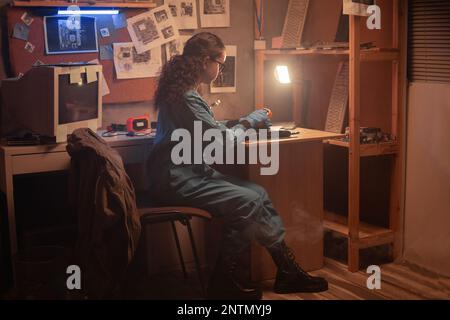 Giovane donna che ripara il computer nel vecchio centro di assistenza. Officina di riparazione computer. Lavorare con un computer portatile rotto in un ufficio buio. Copia Foto Stock