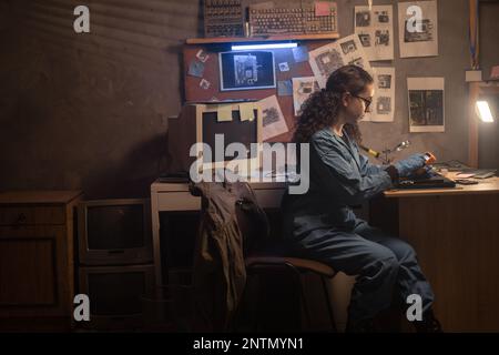Vecchio negozio di riparazione computer. Giovane donna che fissa il circuito stampato nel computer portatile utilizzando un multimetro e diversi strumenti sul tavolo in officina. Tecnologia energetica o engi Foto Stock