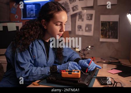 giovane tecnico di computer, un riparatore di schede madri di un laptop sta usando un multimetro per cercare i difetti sulla scheda madre per riparare in vecchia officina. Boa Foto Stock