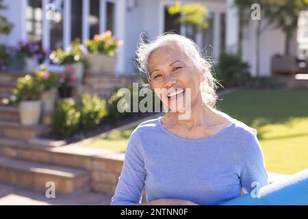 Ritratto di felice donna asiatica anziana con tappetino yoga in giardino Foto Stock