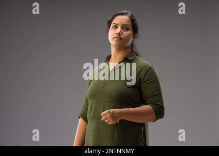 Ritratto di una donna indiana, posa in piedi che mostra diversi gesters, con sfondo grigio, isolato. Foto Stock