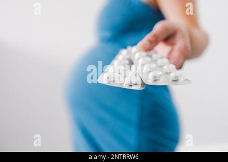 donna incinta che tiene in mano compresse multivitaminiche e che mostra il suo urto nell'ultima fase della gravidanza Foto Stock