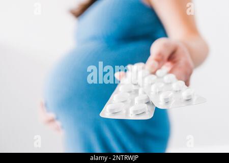 donna incinta che tiene in mano compresse multivitaminiche e che mostra il suo urto nell'ultima fase della gravidanza Foto Stock