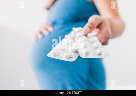 donna incinta che tiene in mano compresse multivitaminiche e che mostra il suo urto nell'ultima fase della gravidanza Foto Stock