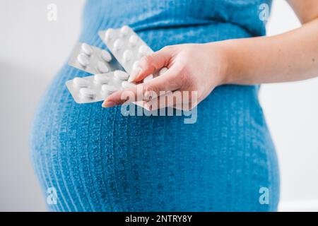 donna incinta che tiene in mano compresse multivitaminiche e che mostra il suo urto nell'ultima fase della gravidanza Foto Stock