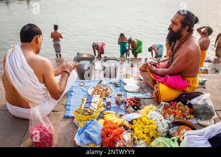 Un Pandits (uomo santo e il sacerdote che compie cerimonie) preparare offerte e pregando, sul ghats del fiume Gange, in background i pellegrini di balneazione, Foto Stock