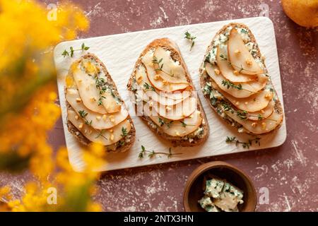 roquefort formaggio francese e pesche affettate tostare su un piatto quadrato, su un tavolo sotto mimosa fiori, vista dall'alto Foto Stock