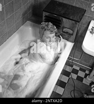 Ascoltatori radio in passato. Una giovane donna nella vasca da bagno che si affaccia alla radio che si siede sul bordo della vasca. Sulla parte anteriore della radio è presente una scala e quando si ruota la manopola accanto ad essa in modo che il puntatore si trovi al centro del nome di una stazione, la stazione era lì. Oltre alle trasmissioni FM, hanno anche ascoltato le radio straniere a onde lunghe. Svezia nel 1945 Kristofferson Ref L180-4,2 Foto Stock