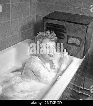 Ascoltatori radio in passato. Una giovane donna nella vasca da bagno che si affaccia alla radio che si siede sul bordo della vasca. Sulla parte anteriore della radio è presente una scala e quando si ruota la manopola accanto ad essa in modo che il puntatore si trovi al centro del nome di una stazione, la stazione era lì. Oltre alle trasmissioni FM, hanno anche ascoltato le radio straniere a onde lunghe. Svezia nel 1945 Kristofferson Ref L180-4 Foto Stock