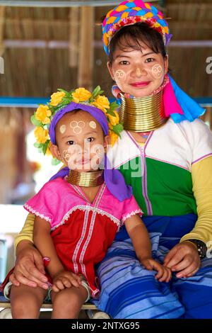 donna della tribù a collo lungo, nota per gli anelli metallici indossati intorno al collo, che tiene il bambino. Foto cattura il legame tra madre e chi Foto Stock