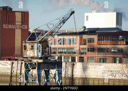 06 febbraio 2023, Amburgo: Edifici ristrutturati di Schaub & Co e Brandshof 68 dietro una ex gru di carico a Billhafen. Il porto e gli edifici adiacenti sono testimonianze architettoniche dell'ex porto libero di Amburgo, così come l'adiacente Zollhallen Veddel. Foto: Soeren Stache/dpa Foto Stock