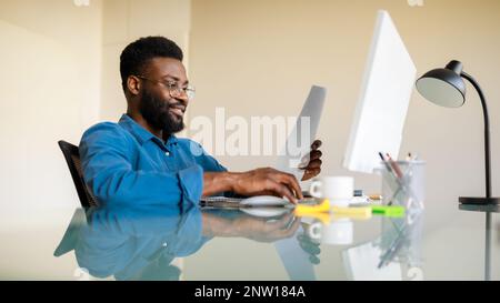 Imprenditorialità di successo. Buon uomo d'affari nero che controlla i documenti finanziari, seduto alla scrivania in ufficio, panorama Foto Stock