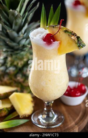 Cocktail Pina colada guarnito con ciliegia, fettina di ananas e foglie su un piatto di legno Foto Stock