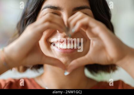 Felice giovane donna araba mostrando cuore Gesture con le mani e sorridente, Closeup Foto Stock