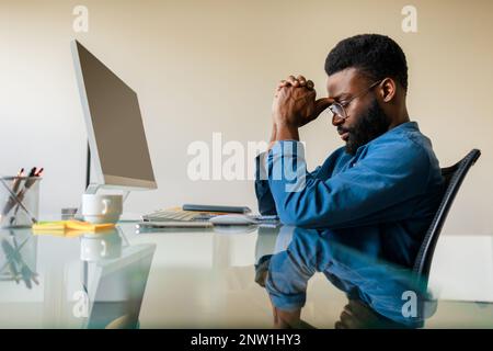 Arrabbiato uomo d'affari nero penoso seduto alla scrivania con computer, analista professionista maschio pensiero di soluzione del problema Foto Stock