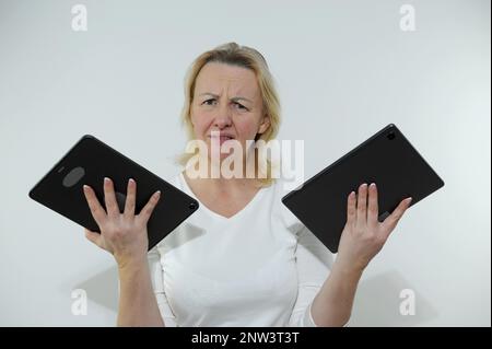 Donna ha due compresse in mani è infelice guarda in frame stanco del lavoro una sovrabbondanza di informazioni bruciate sul lavoro sfondo bianco abiti Studio bianco non tinti capelli non tempo per te Foto Stock