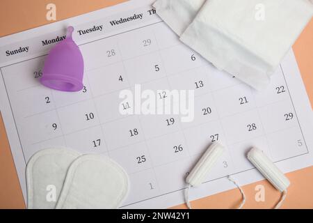 Composizione piatta con calendario e tamponi mestruali su sfondo arancione chiaro Foto Stock