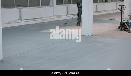 Lavoratore dipinge il pavimento di calcestruzzo con vernice grigia liquida Foto Stock