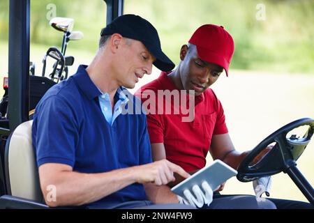 Ottenere i migliori consigli di golf online. Scatto di due uomini in un golf cart guardando un tablet digitale. Foto Stock