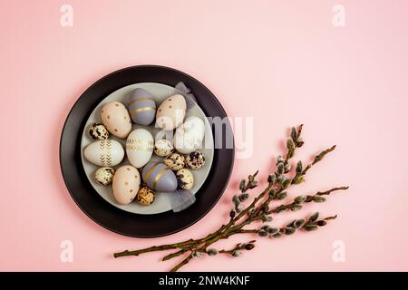 Piatti con uova di Pasqua dipinte e rami di salice su sfondo rosa. Biglietto di auguri di Pasqua. Vista dall'alto, disposizione piatta, spazio di copia. Foto Stock