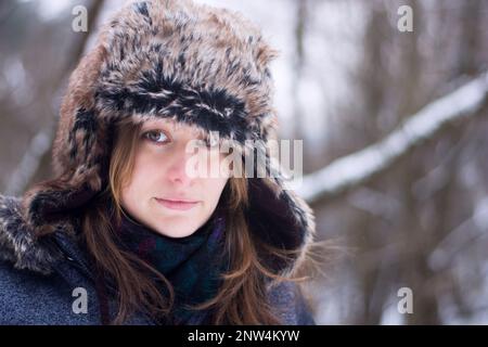 Giovane donna caucasica in cappello e cappotto d'inverno. Foto di Headshot nella foresta innevata in inverno. Foto Stock