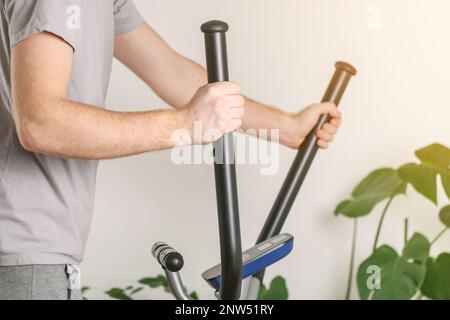 Un uomo si allena su una macchina ellittica. Allenatore sportivo a casa in appartamento. Sport a casa. Foto Stock
