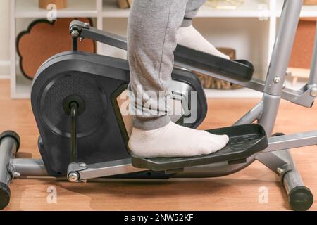 Un uomo si allena su una macchina ellittica. Allenatore sportivo a casa in appartamento. Sport a casa. Foto Stock