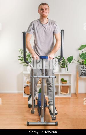 Un uomo si allena su una macchina ellittica. Allenatore sportivo a casa in appartamento. Sport a casa. Foto Stock