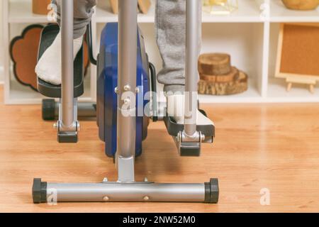 Un uomo si allena su una macchina ellittica. Allenatore sportivo a casa in appartamento. Sport a casa. Foto Stock