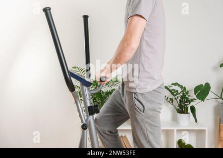 Un uomo si allena su una macchina ellittica. Allenatore sportivo a casa in appartamento. Sport a casa. Foto Stock