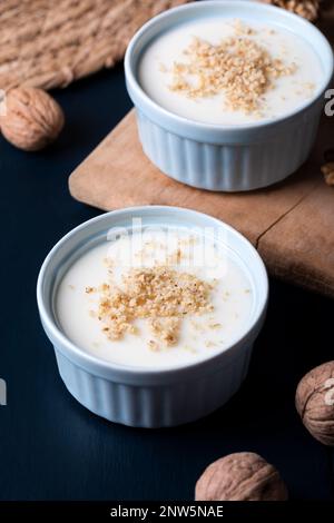 Crema pasticcera fatta in casa con noce, dessert turchi muhallebi su uno sfondo di legno. Crema fatta in casa con noce. Foto Stock