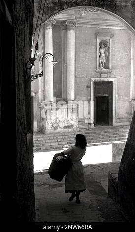 Una giovane donna italiana porta un cesto attraverso le deserte le strade di Roma, Italia negli anni trenta del novecento, eventualmente sul suo modo di mercato. Foto Stock