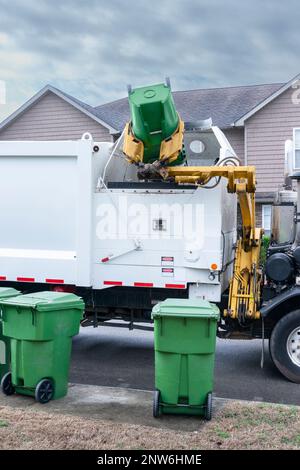 Colpo verticale di un camion di rifiuti meccanizzato che scarica i rifiuti dal barile residenziale. Foto Stock