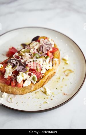 Dakos insalata tradizionale greca insalata con fette biscottate di orzo o pane ammollato e croccante, condita con pomodori succosi, formaggio feta, cipolle, olive, e un Foto Stock